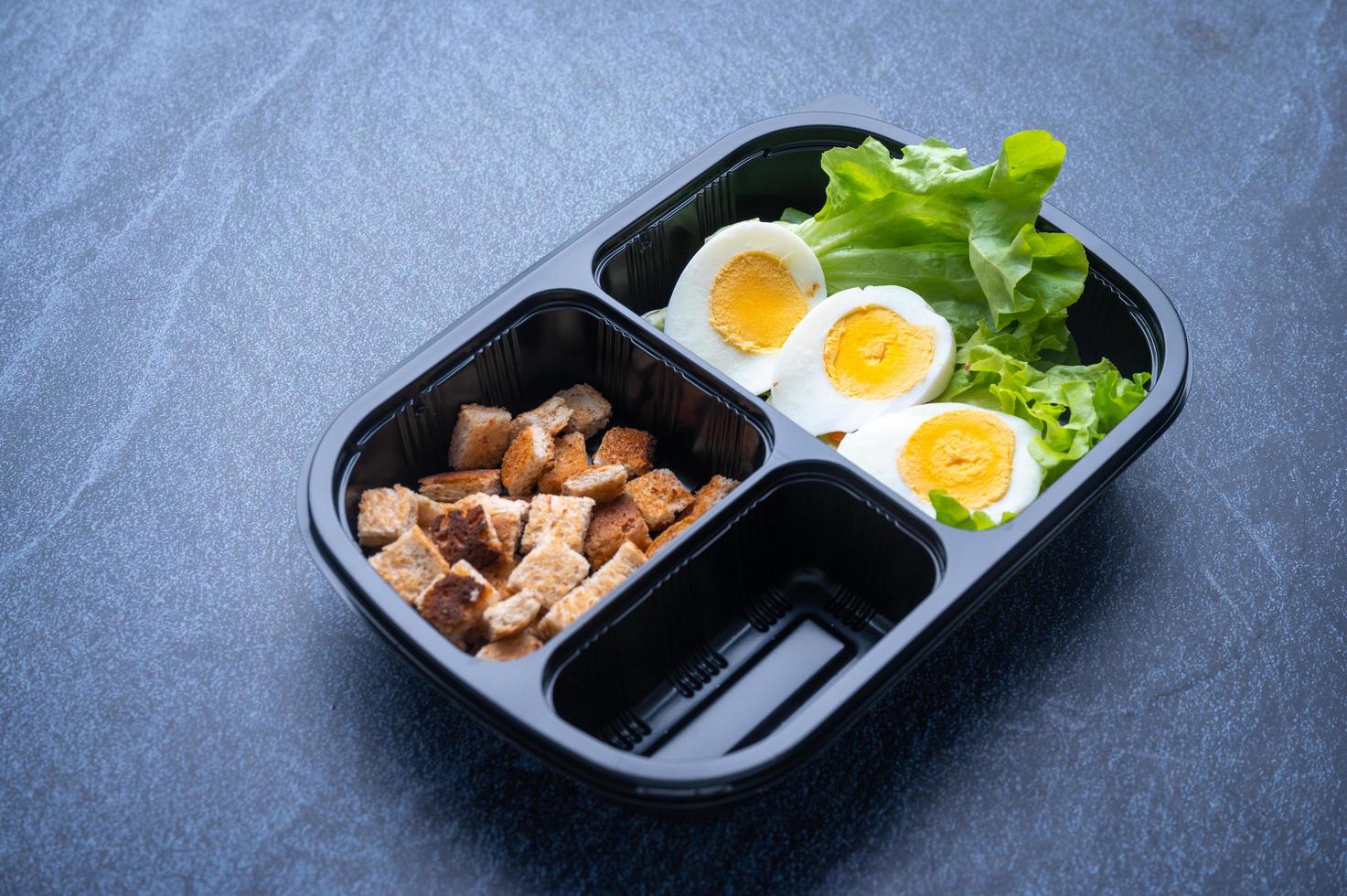 Sectioned plastic food container with croutons, lettuce, and sliced hard-boiled egg photo