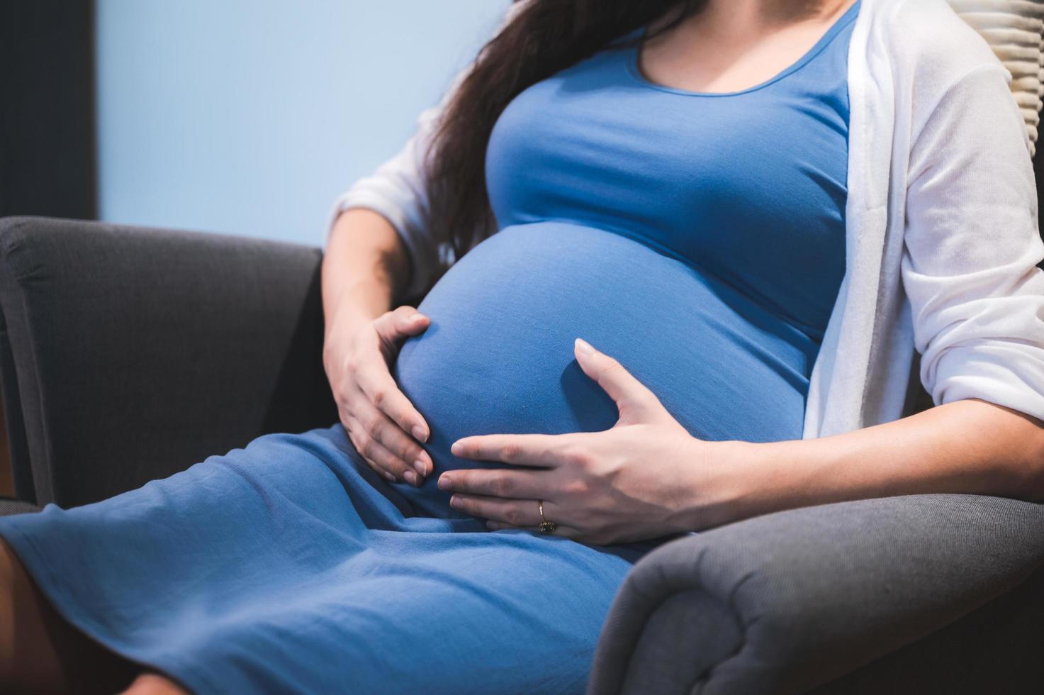 Pregnant woman wearing blue dress with her hands on her stomach photo