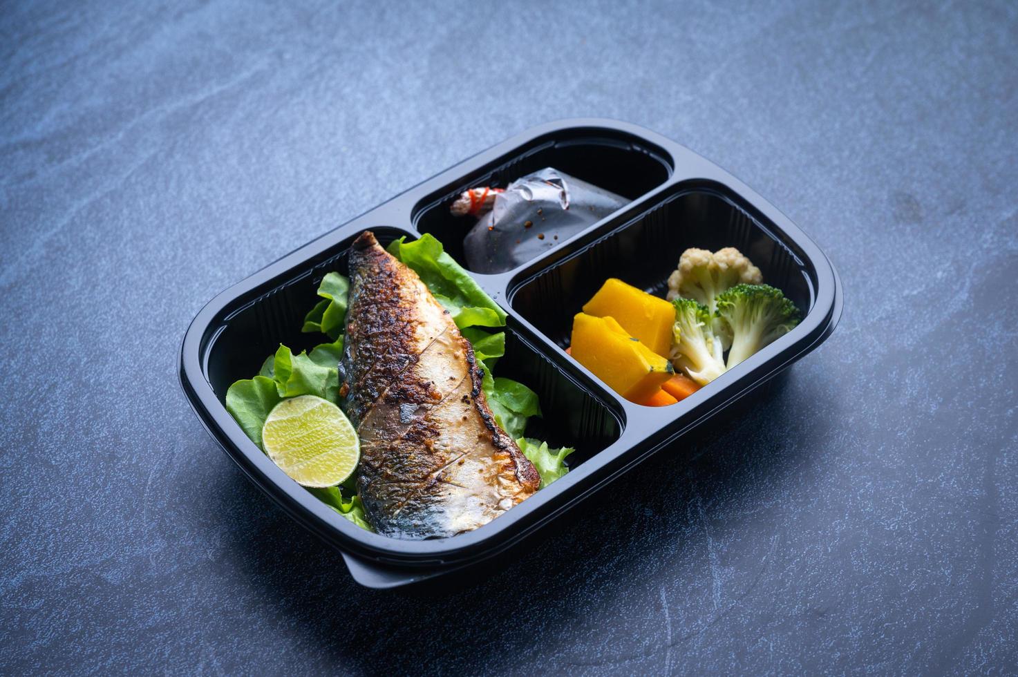 Sectioned plastic food container with salad, grilled fish, and vegetables photo