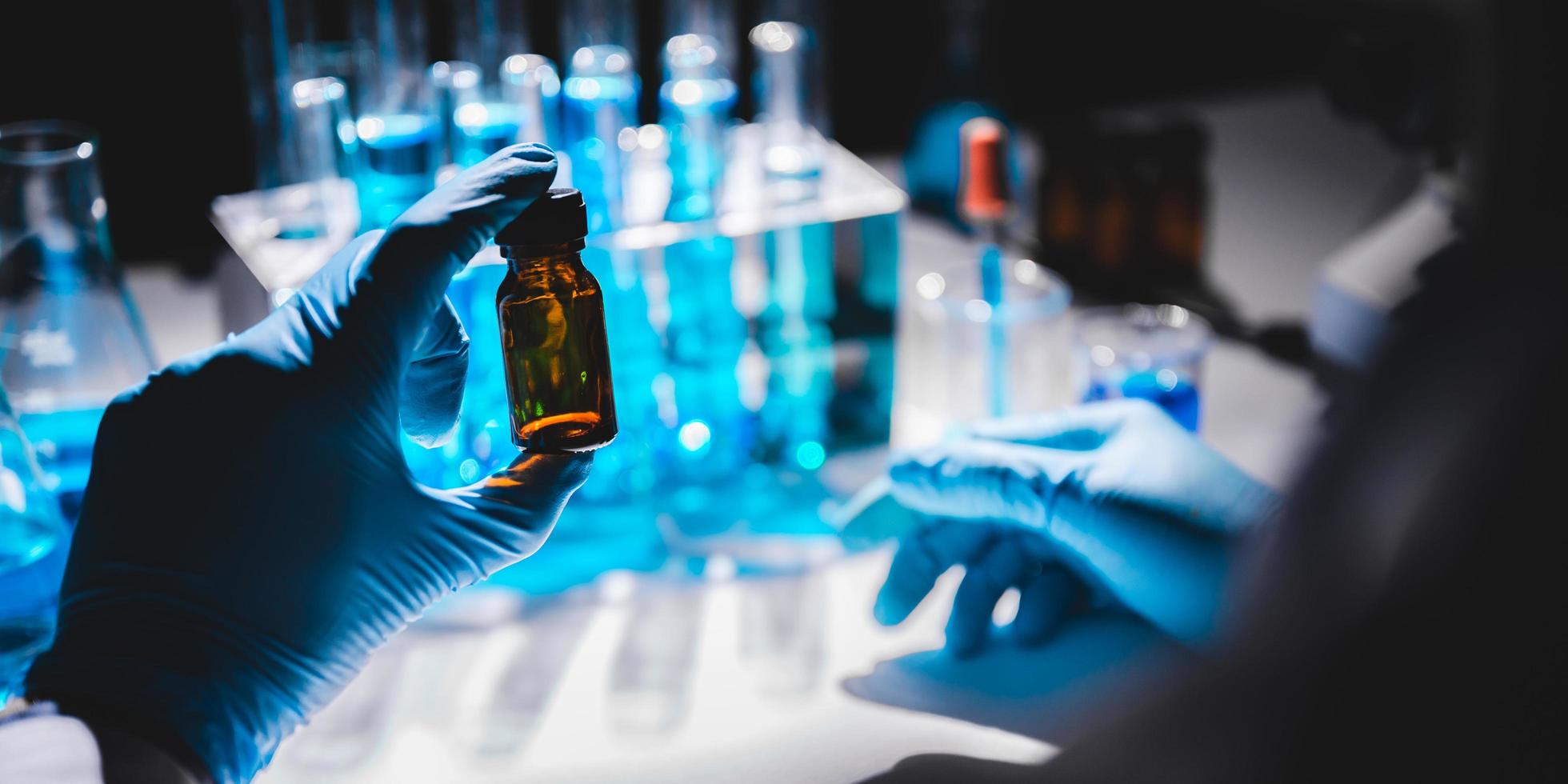 Hand in blue glove holding vial with vials of blue liquid in the background photo