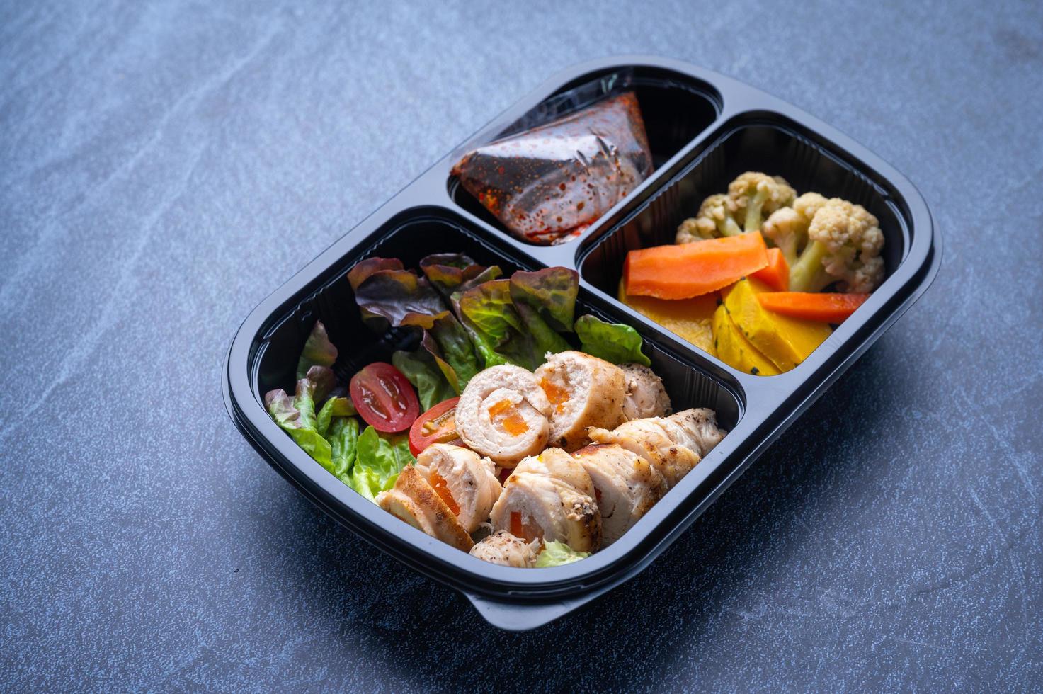 Sectioned plastic food container with salad, sliced meat, and vegetables photo