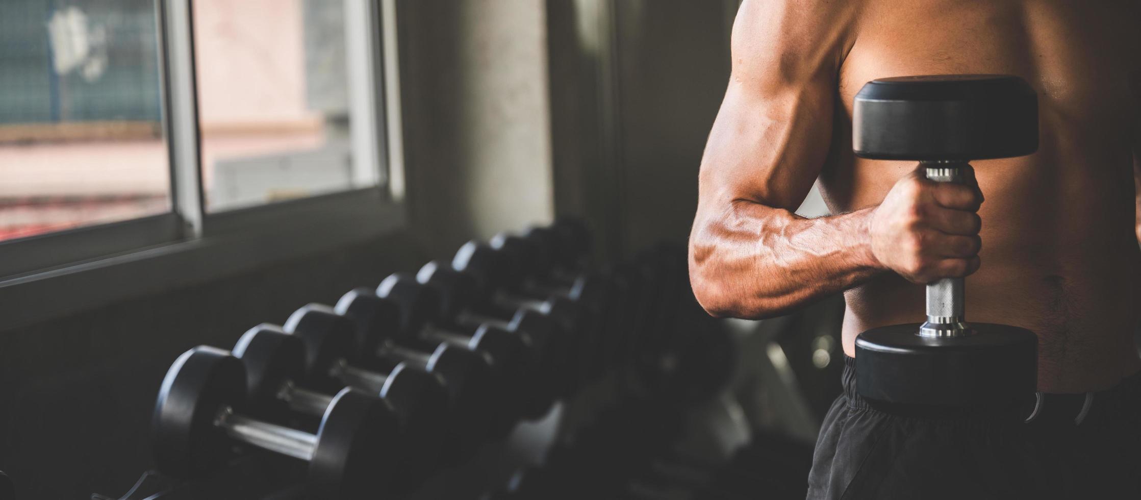 Hombre sujetando una pesa en un gimnasio con una fila de pesas en el fondo foto