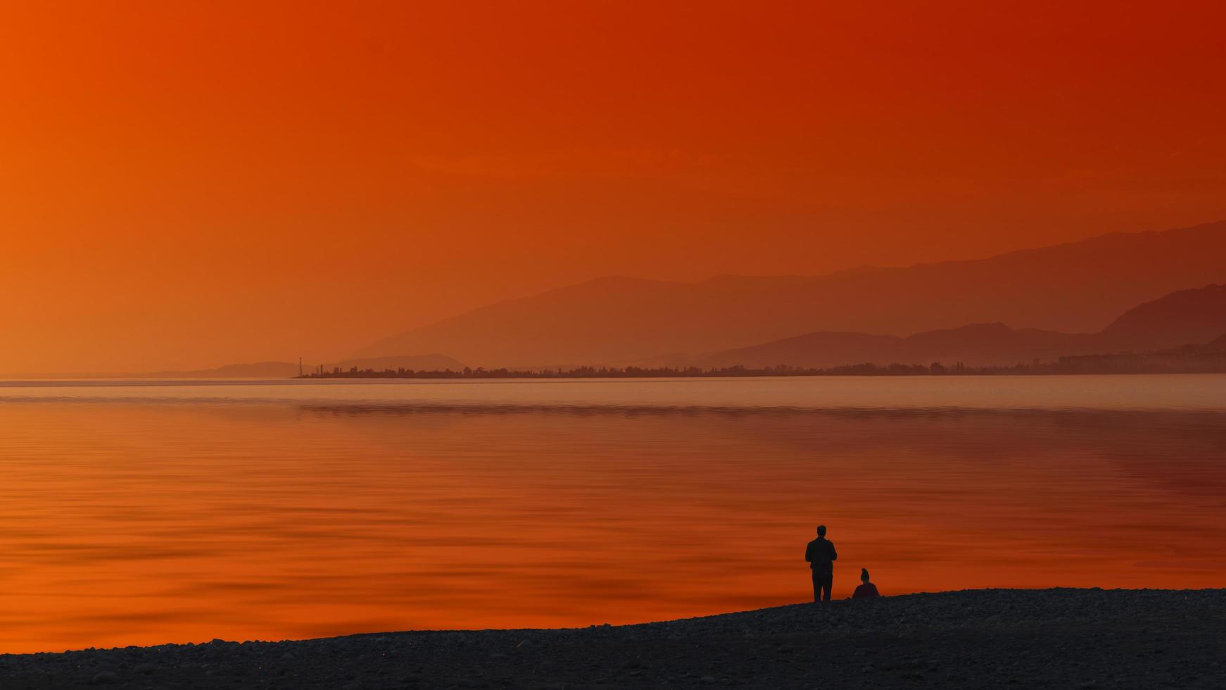 Seascape with orange sunset and silhouettes of people on the beach photo