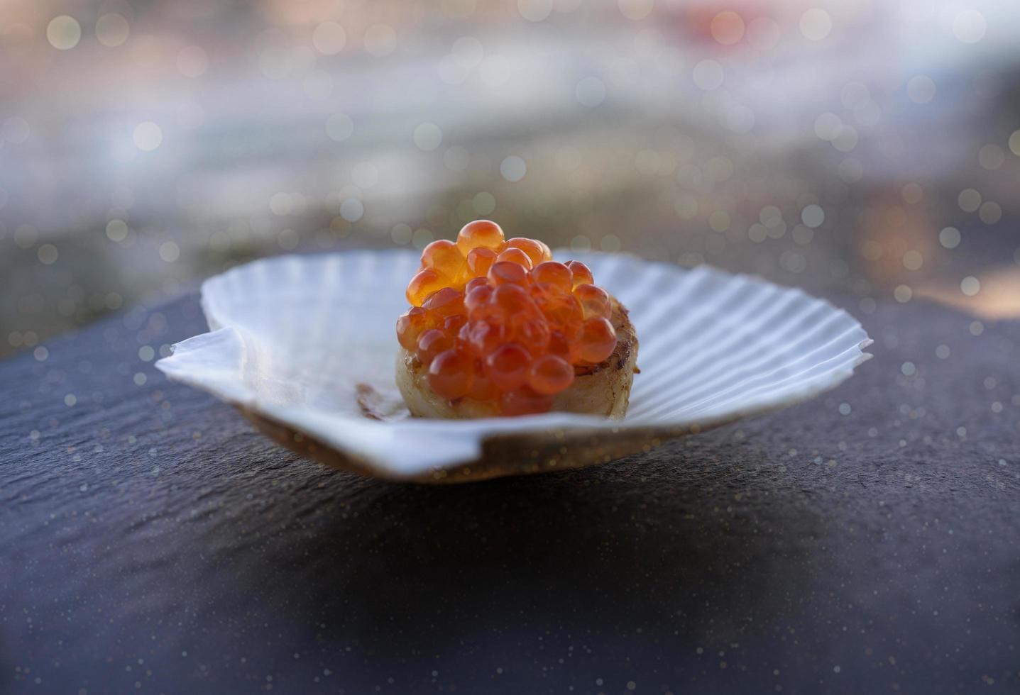 Red caviar on a scallop fillet on a white porcelain shell plate on table photo