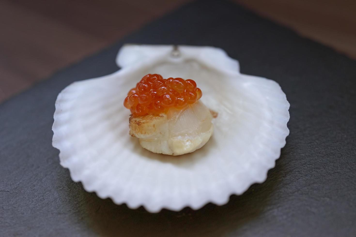 Caviar rojo sobre un filete de vieira sobre una placa de concha de porcelana blanca sobre la mesa foto
