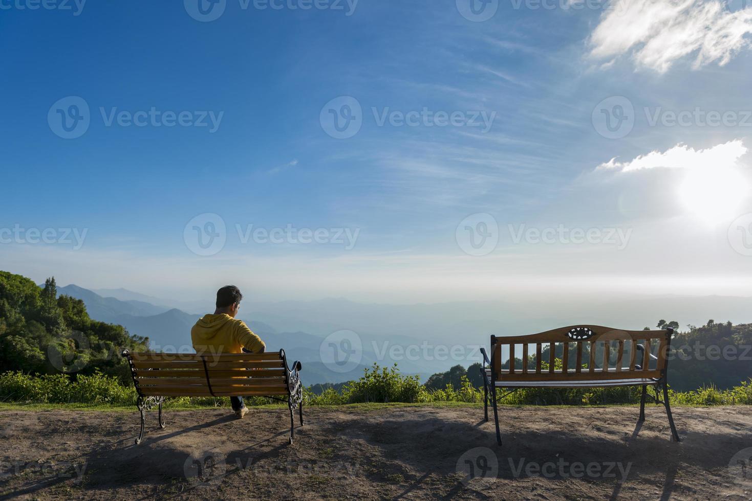 Hombre viajero sentado en un banco de madera con fondo de montaña foto