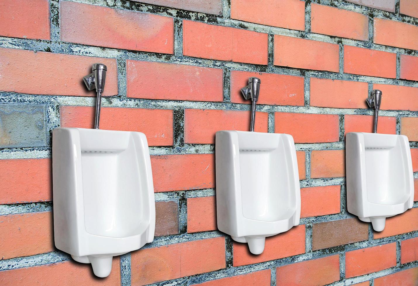 Three urinals against brick wall photo