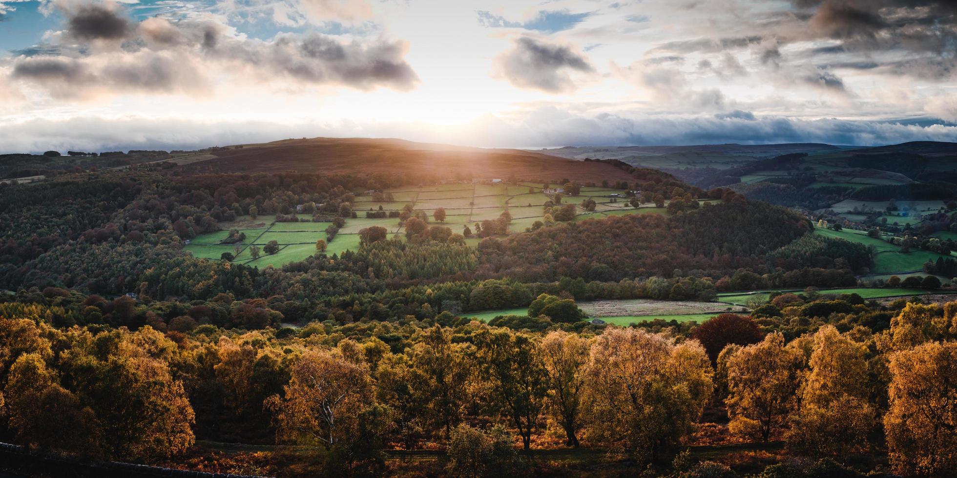 Aerial view of colorful trees in hills with low sun in cloudy blue sky photo