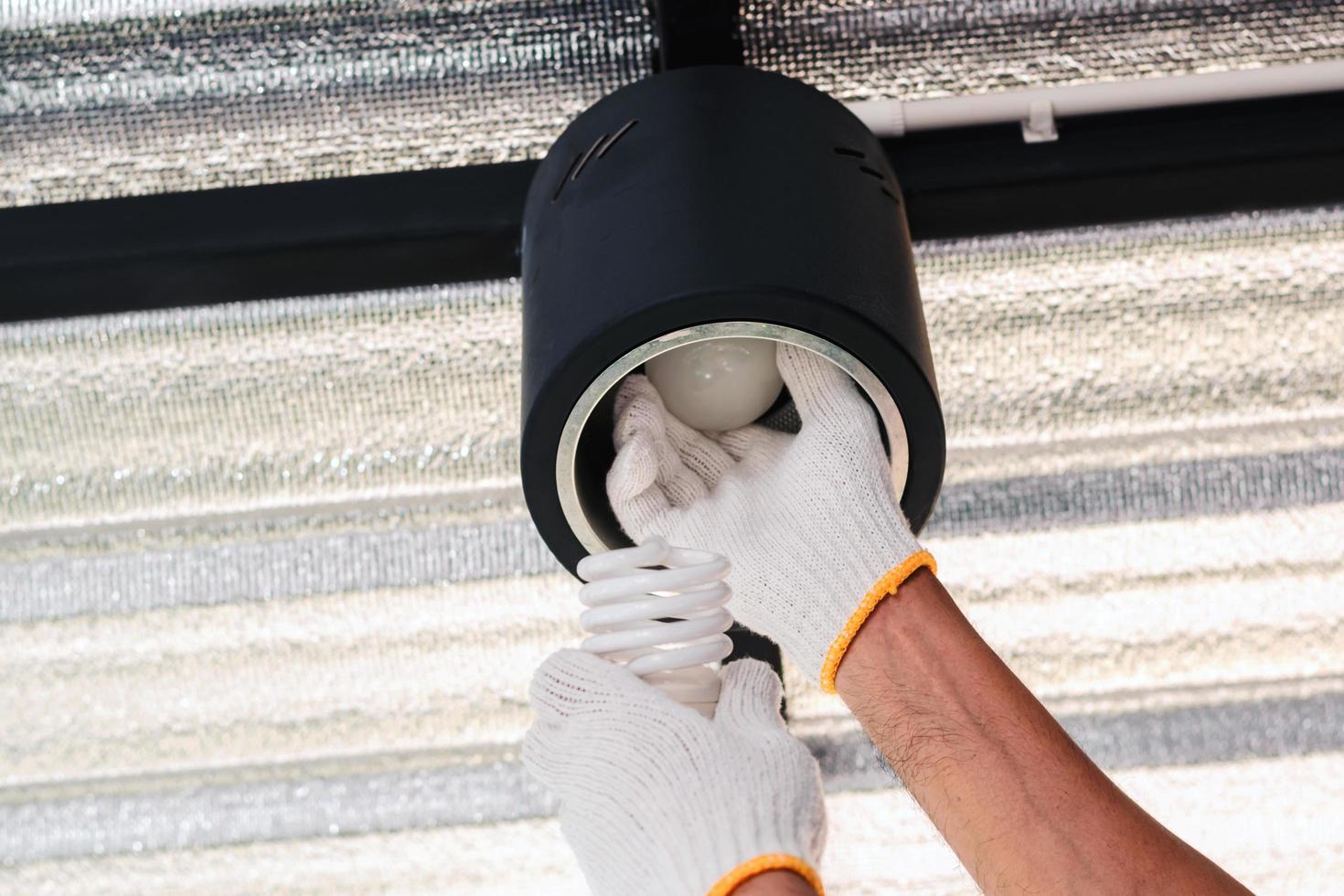 Two hands in gloves replacing a fluorescent bulb with LED bulb photo