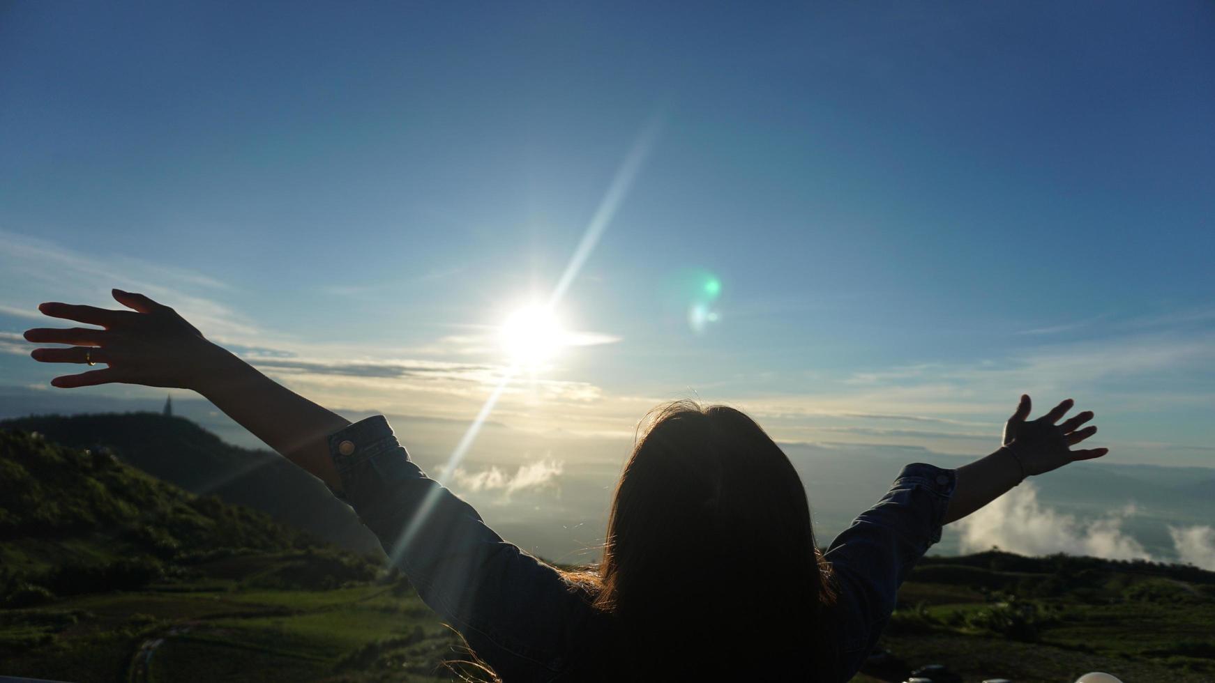 Woman with arms outstretched on top of mountain with cloudy blue sky photo
