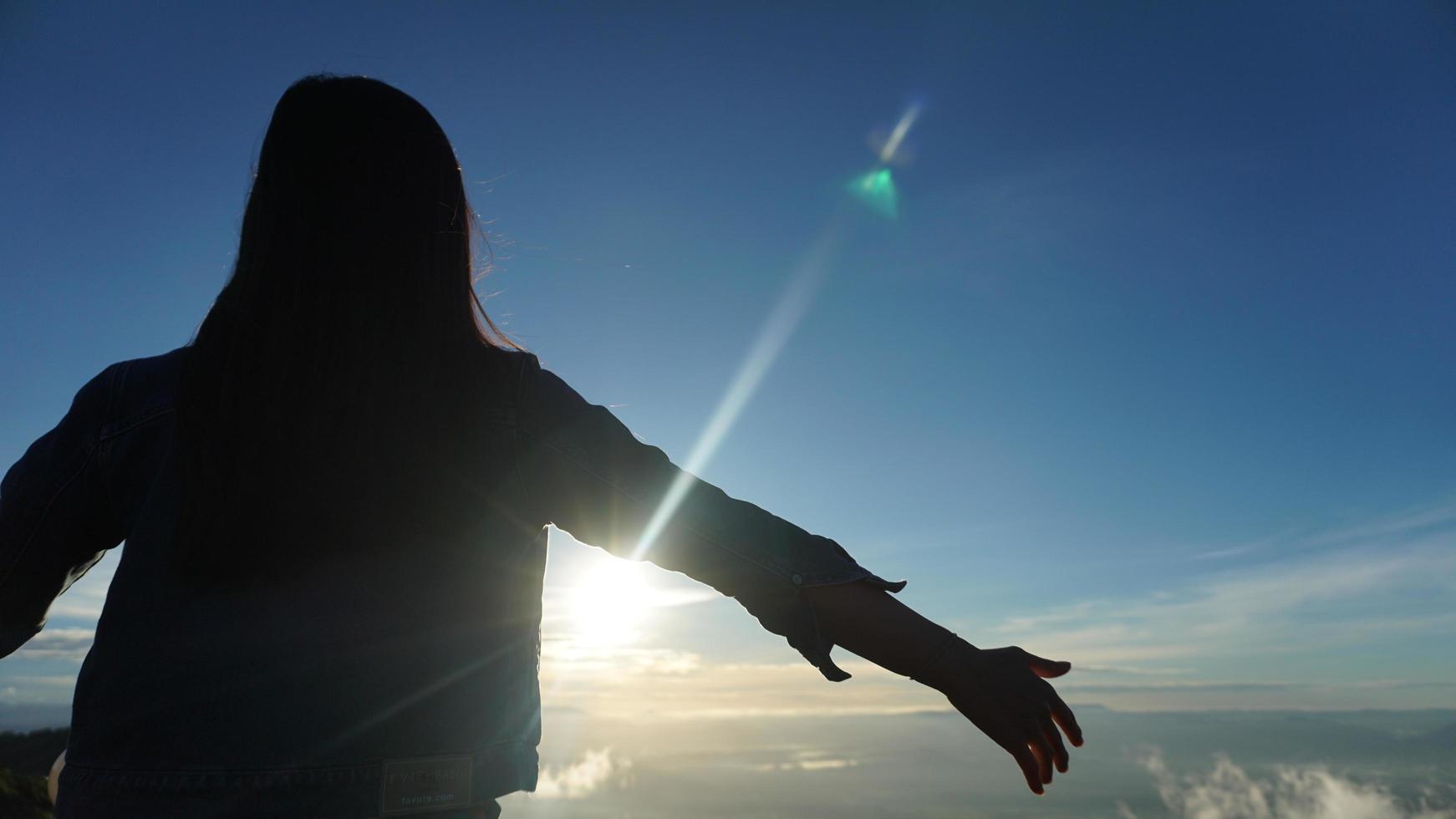 Woman with arms outstretched on top of a mountain with cloudy blue sky photo