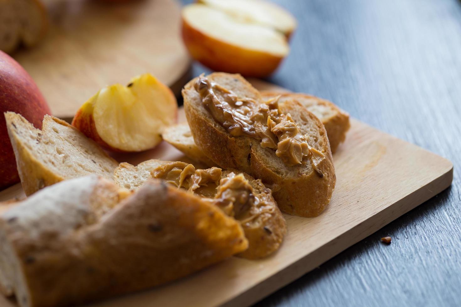 Manzanas en rodajas con baguette en rodajas con mantequilla de chocolate sobre una placa de madera sobre una mesa de madera oscura. foto