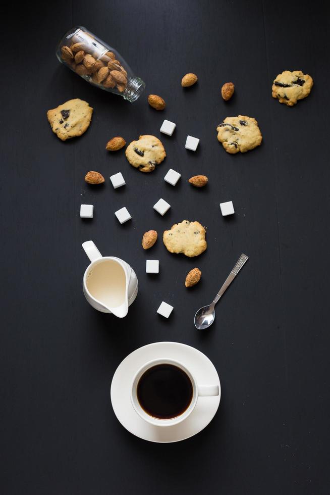 Cup of coffee, saucer, and cream server with pastries on black table photo