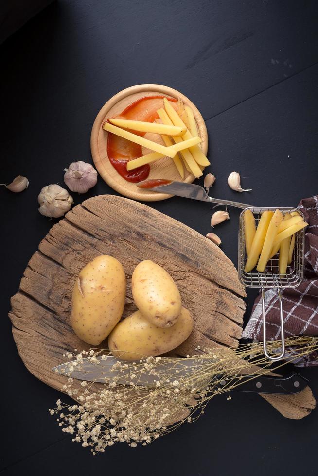 Potatoes on wooden board next to French fries on black table photo