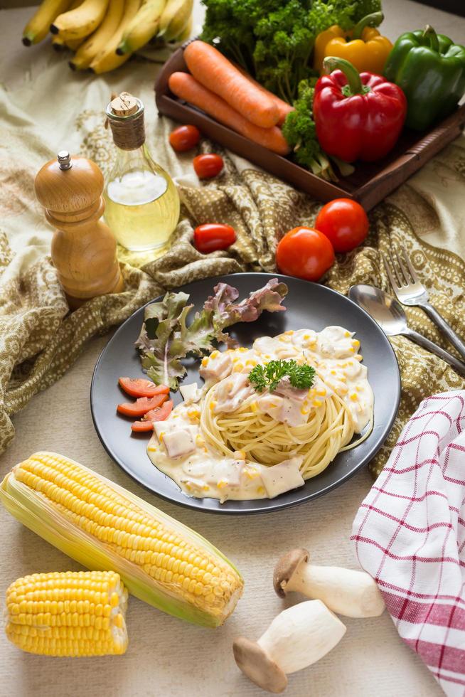 pasta carbonara con tocino y parmesano, lechuga y tomates en rodajas sobre un plato negro foto