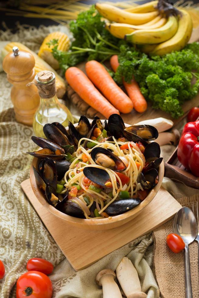 espaguetis y mejillones en un recipiente de madera sobre una tabla de madera junto a verduras foto