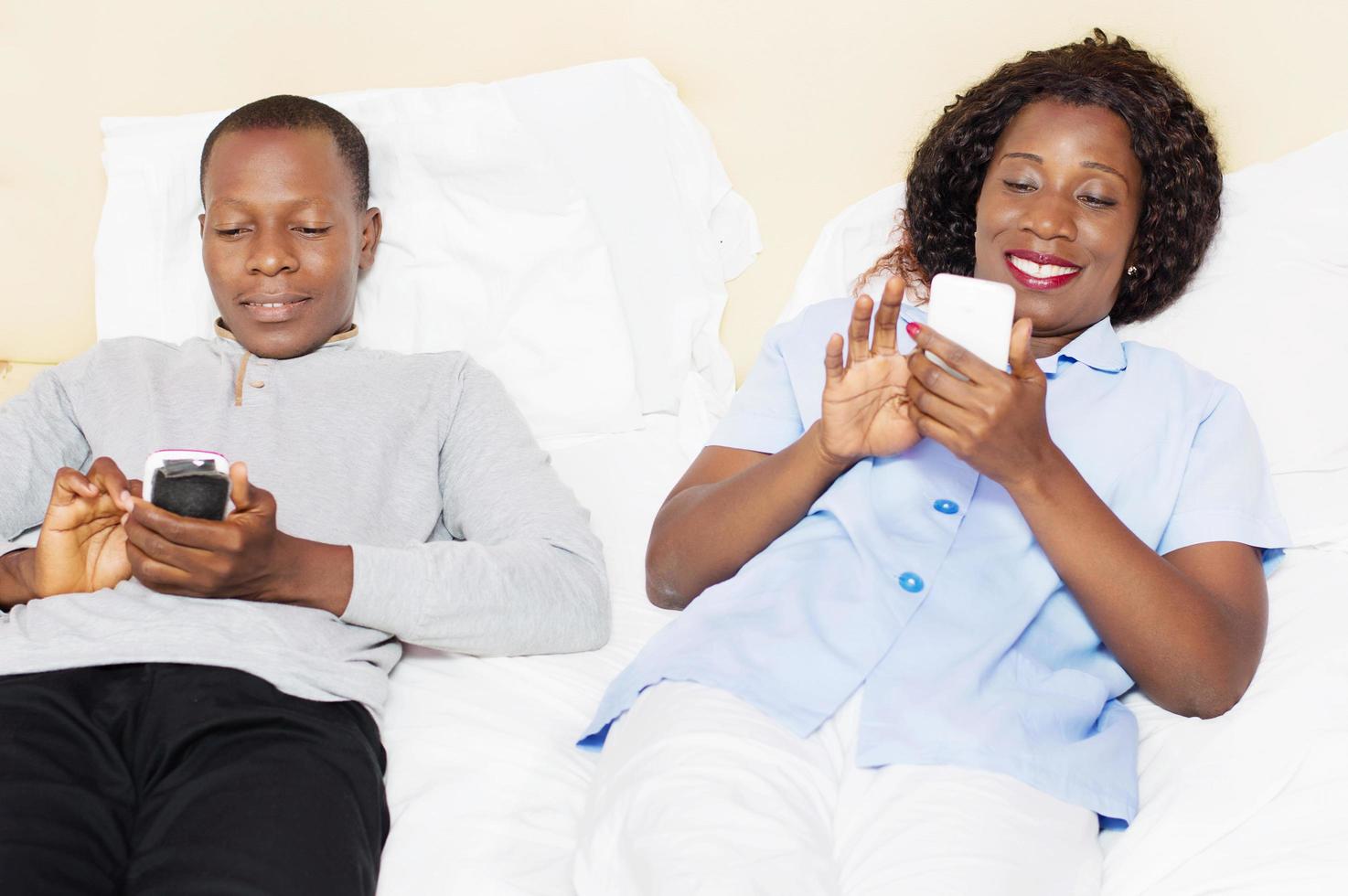 sonriente, pareja joven, utilizar, teléfonos móviles, en cama foto