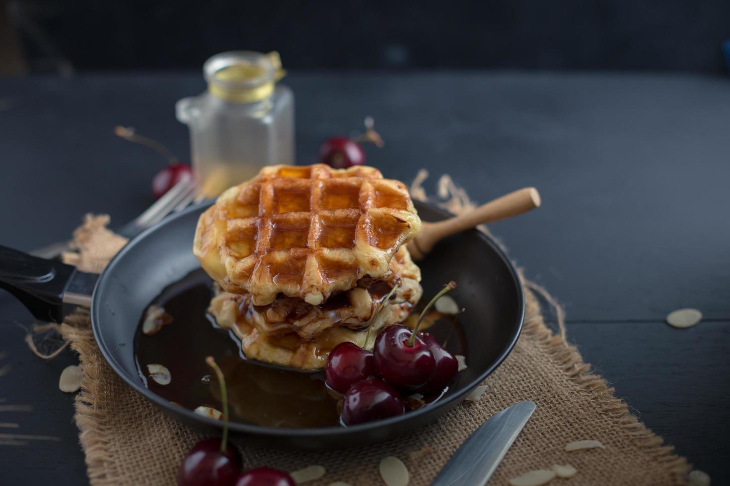 Honey on waffles in a pan with cherries on dark wooden table photo