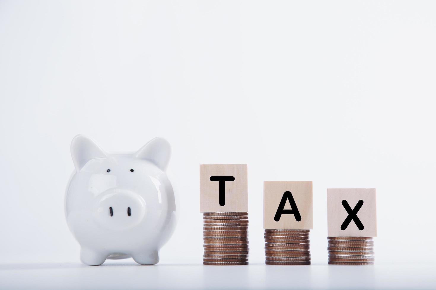 Time to pay tax. Piggybank clock, stacked coins, and wooden block on white background. Taxation and annual tax concept photo