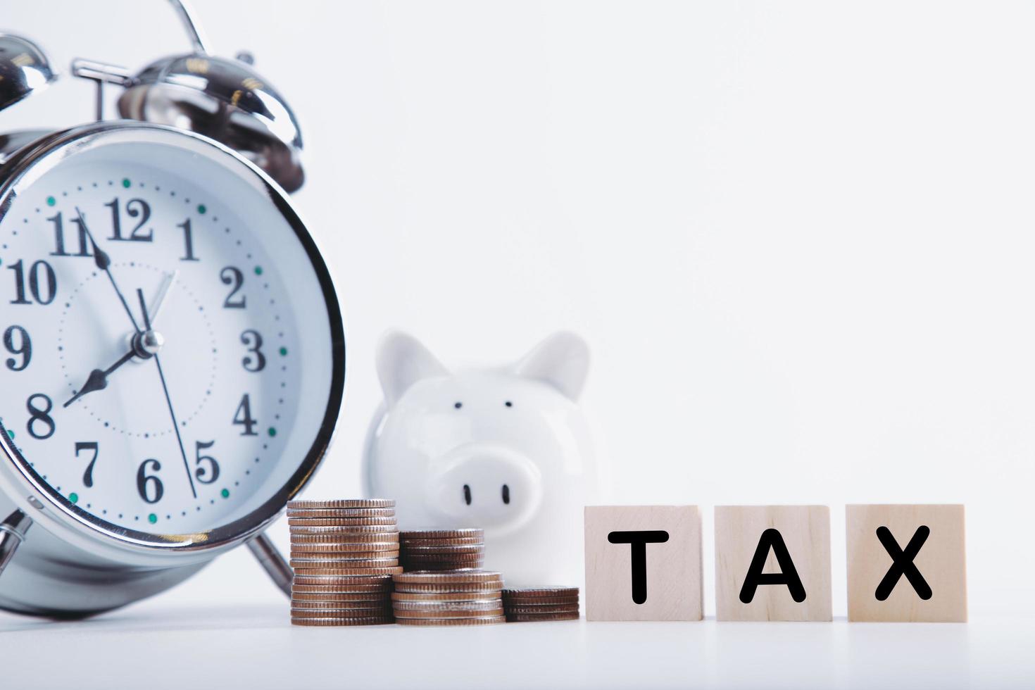 Time to pay tax. Piggybank clock, stacked coins, and wooden block on white background. Taxation and annual tax concept photo