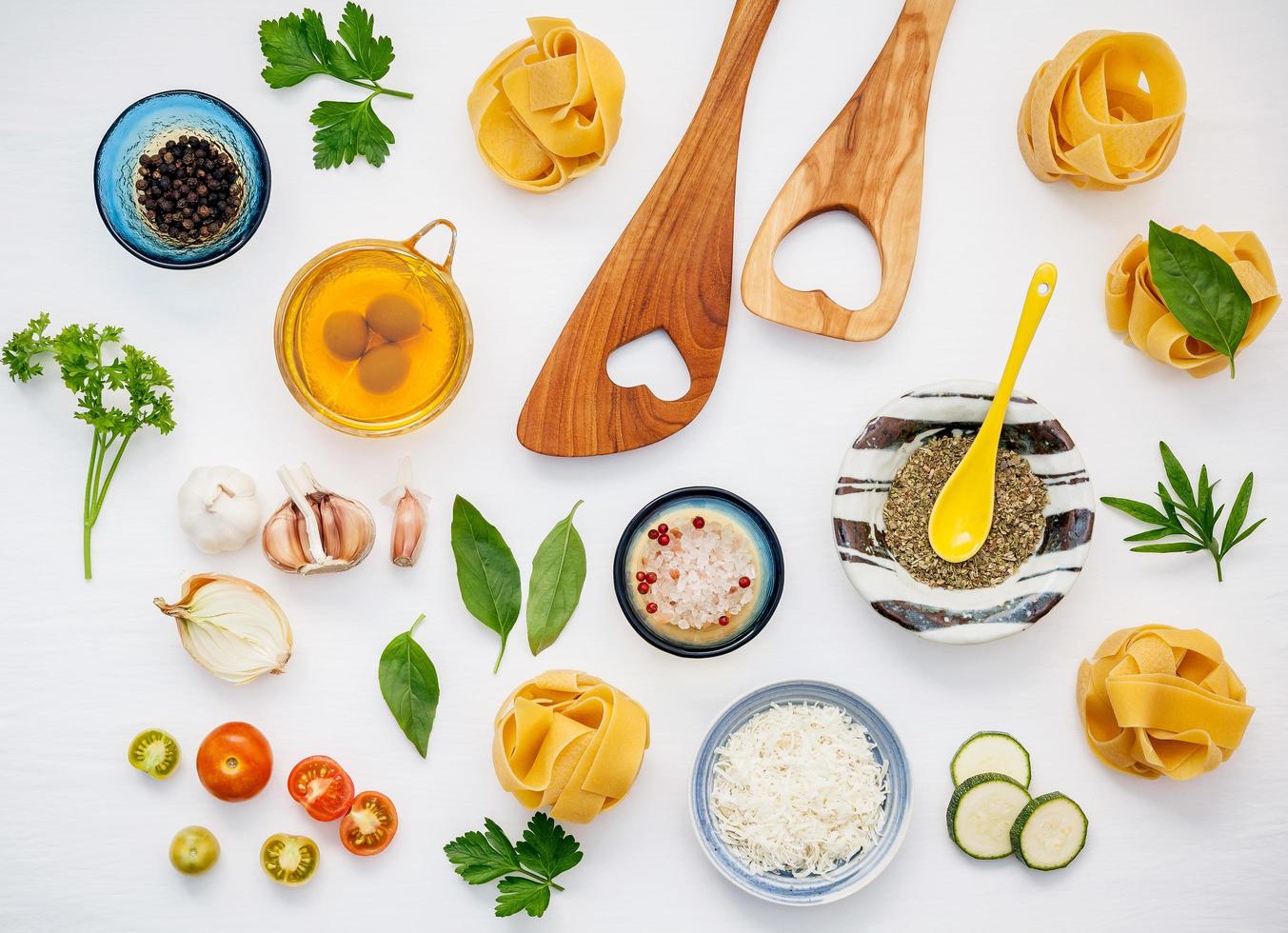 Italian foods concept and menu design. Dried homemade Fettuccine with heart shaped wooden spatula and  ingredients sweet basil ,tomato ,garlic ,parsley ,bay leaves ,pepper ,zucchini and parmesan cheese flat lay. photo