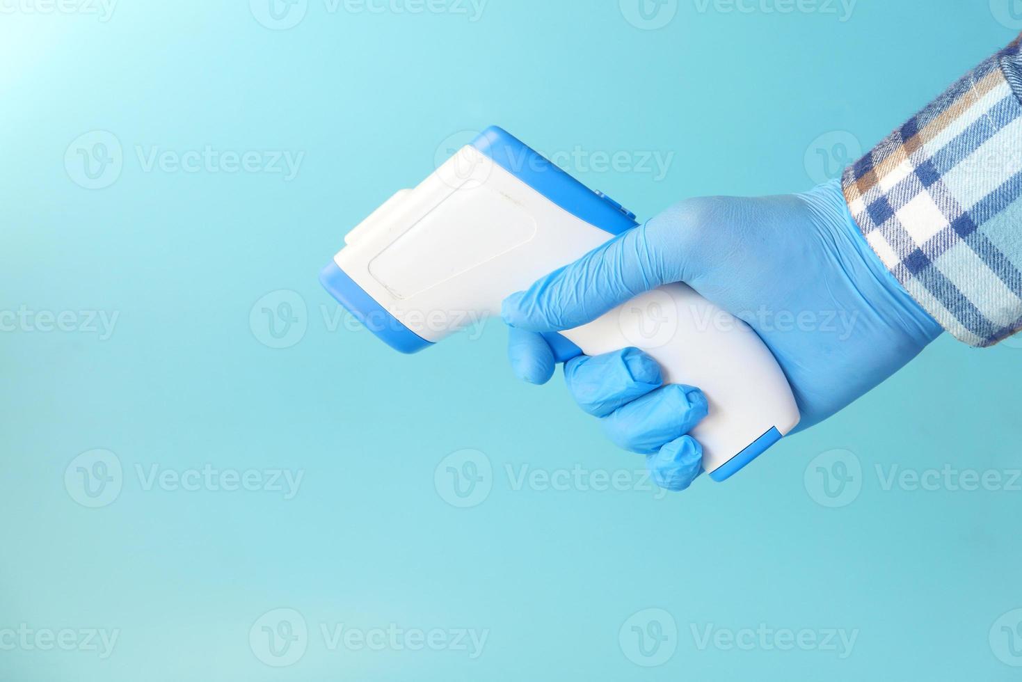 Hand holding infrared thermometer on blue background photo