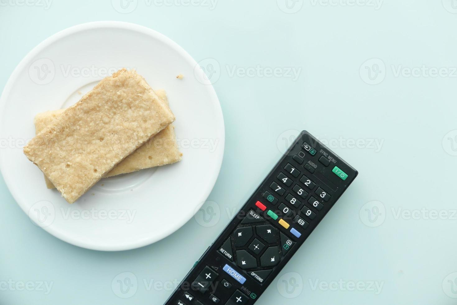 Cookies and tv remote on light blue background photo