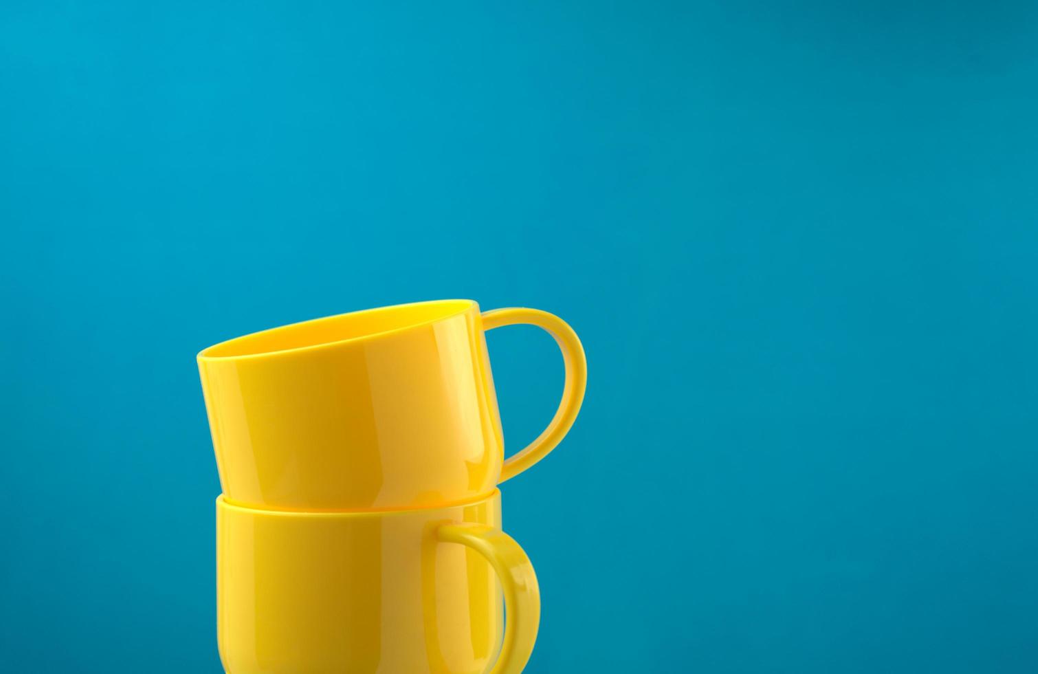 Tazas de color amarillo brillante apiladas sobre fondo azul. foto