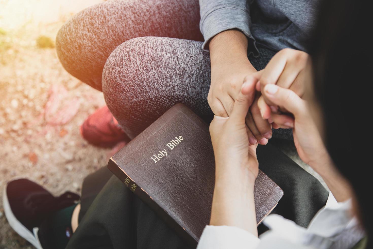 Two women holding hands and praying as they study the bible photo