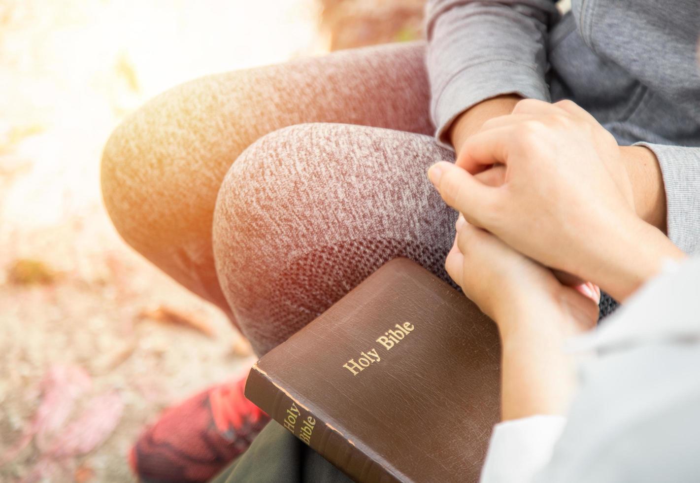 Two women holding hands and praying as they study the bible photo