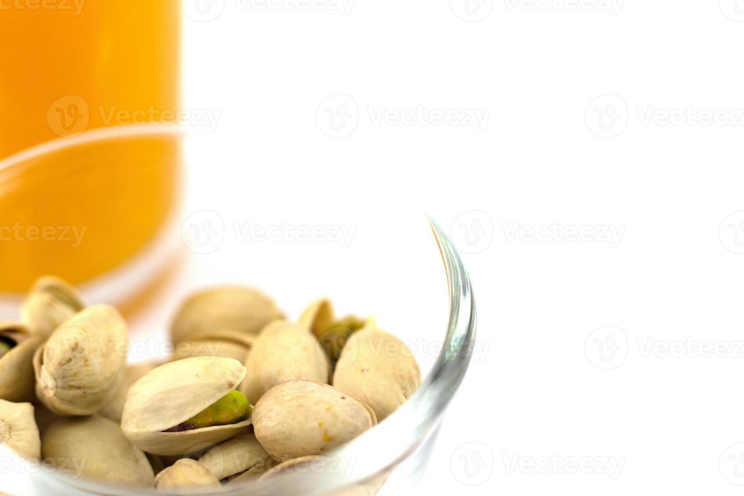 Pistachos en una placa de vidrio y un vaso de jugo de naranja aislado en blanco foto