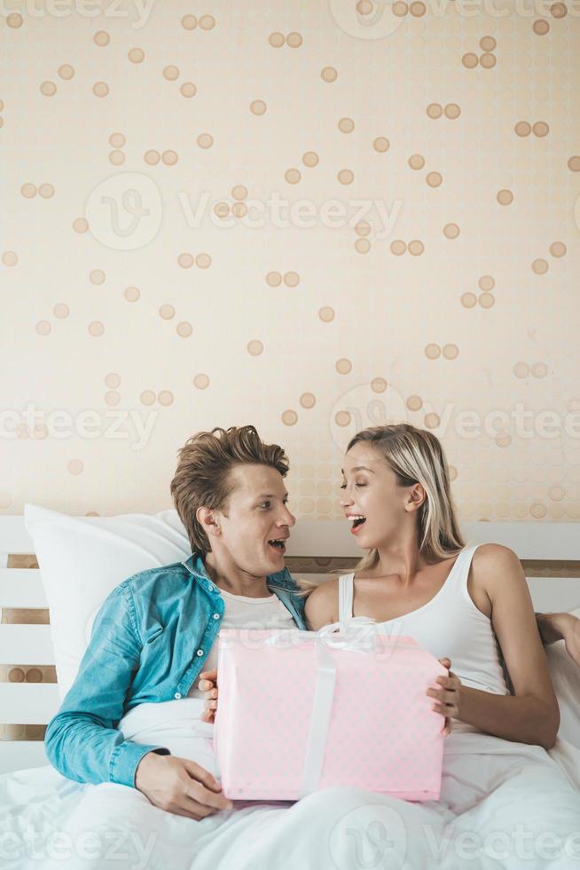 novio sorprende a su novia con una caja de regalo en la cama foto