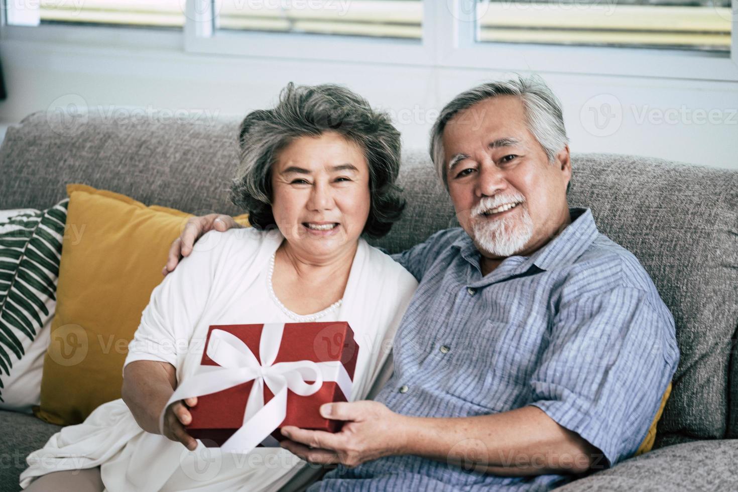 Elderly couple surprises with gift box in living room photo