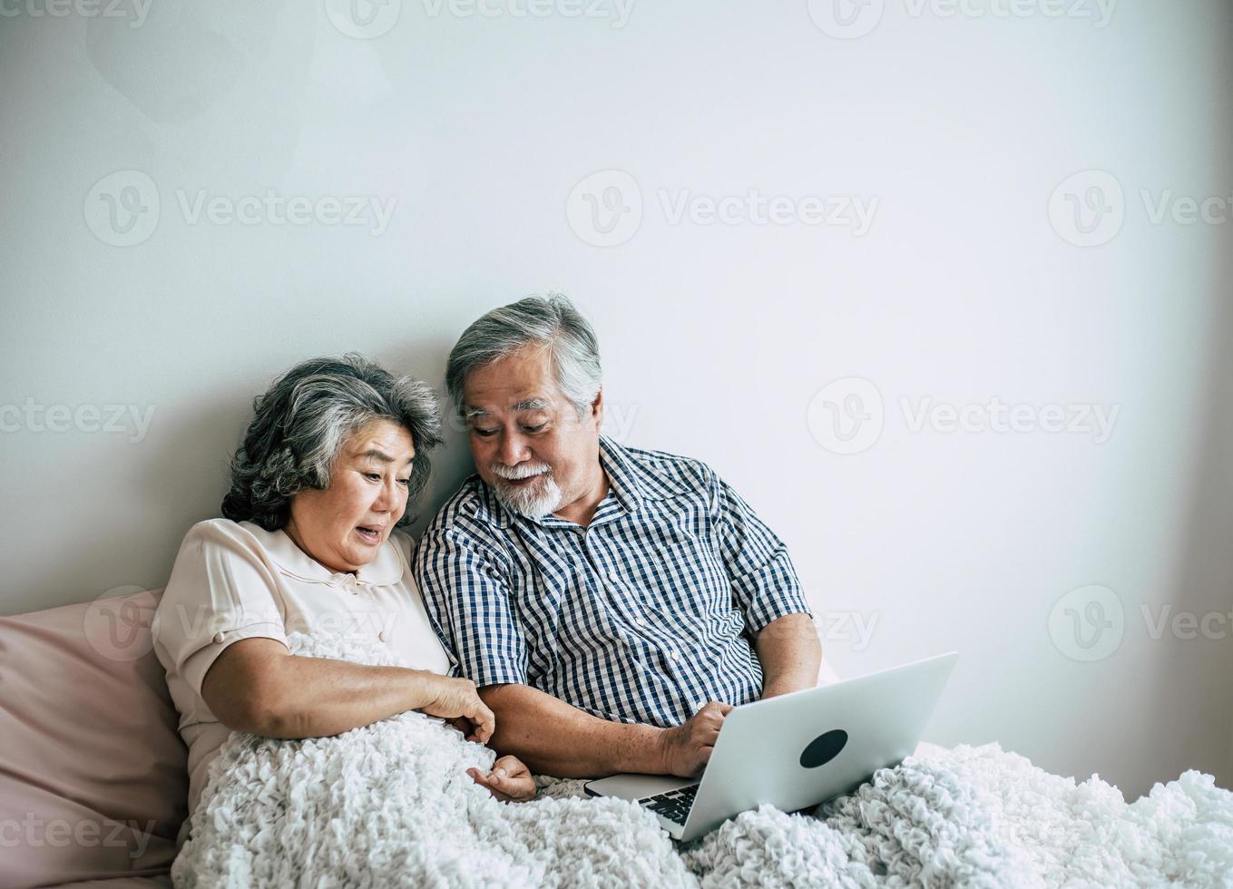 pareja de ancianos hablando y usando la computadora portátil en el dormitorio foto