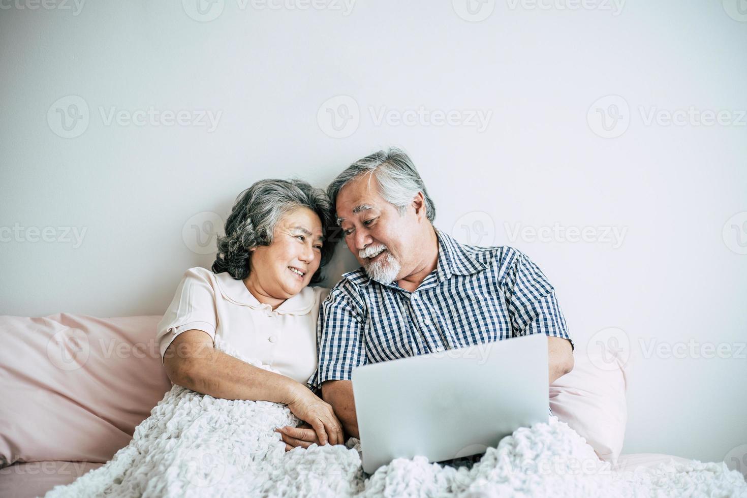 pareja de ancianos hablando y usando la computadora portátil en el dormitorio foto