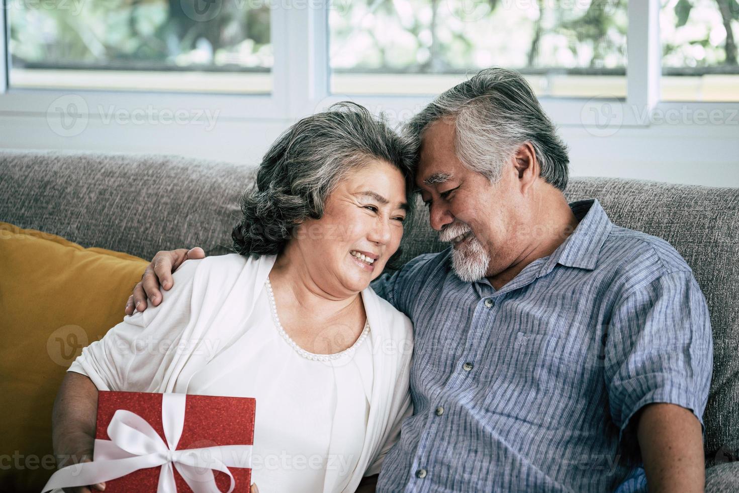 Elderly couple surprises with gift box in living room photo