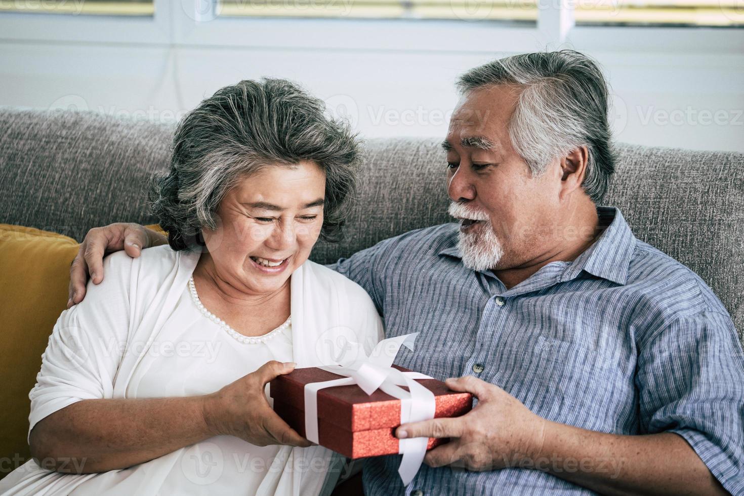 Elderly couple surprises with gift box in living room photo