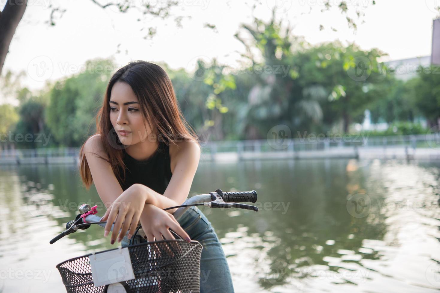 Beautiful young woman riding bicycle in green park photo