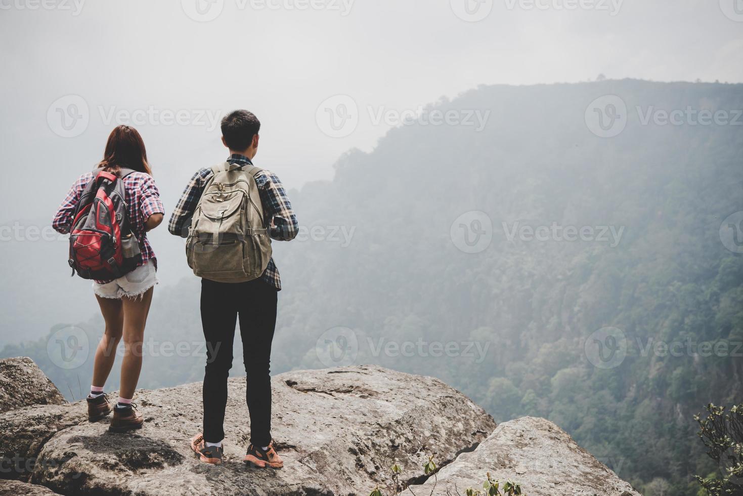 Pareja de excursionistas con mochilas de pie en la cima de una montaña y disfrutando de la vista de la naturaleza foto