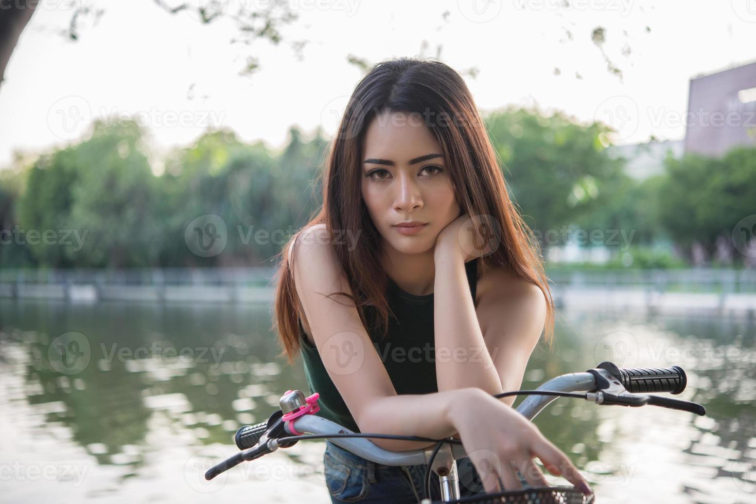 Beautiful young woman riding bicycle in green park photo