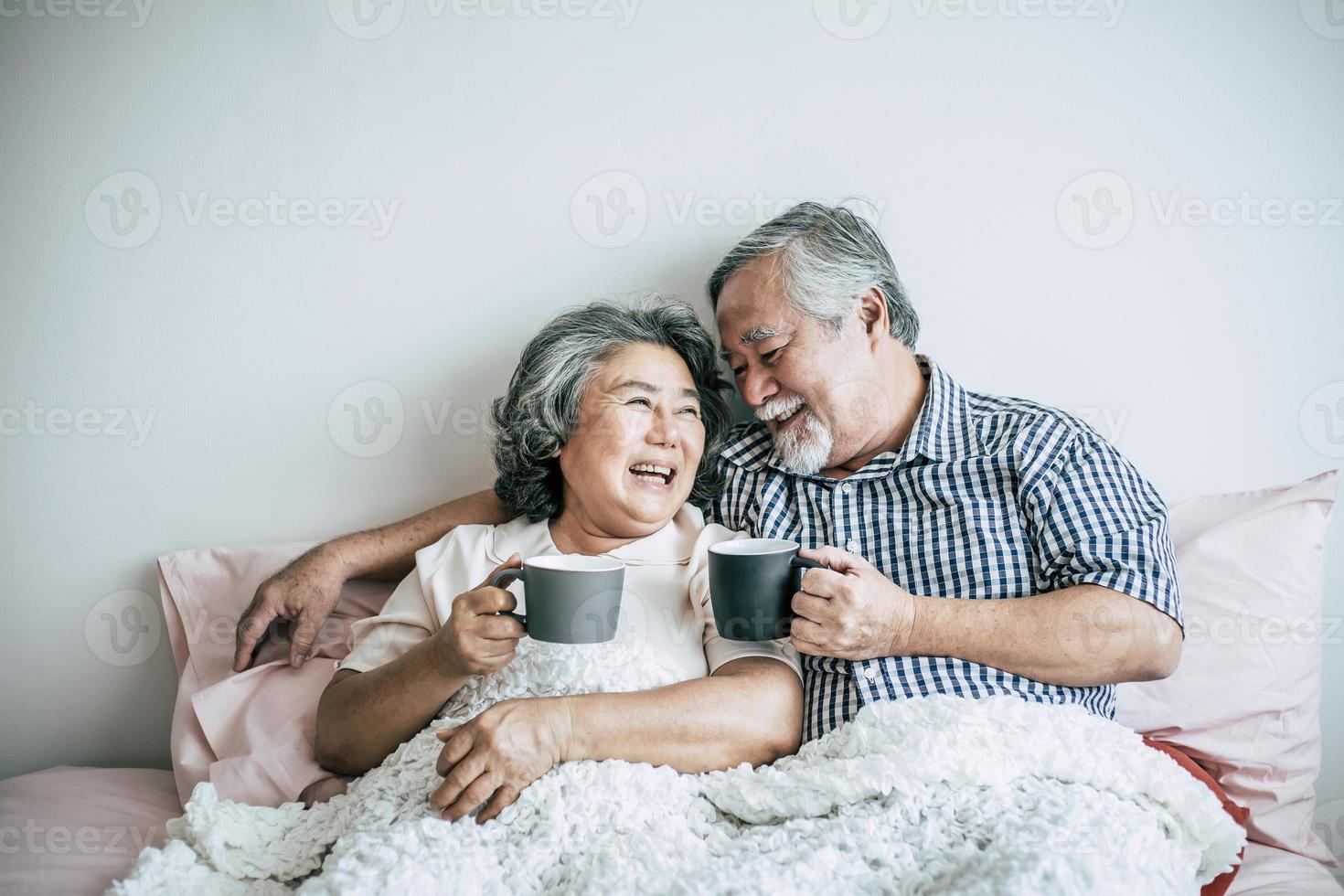 Senior couple laughing while drinking coffee in bedroom photo
