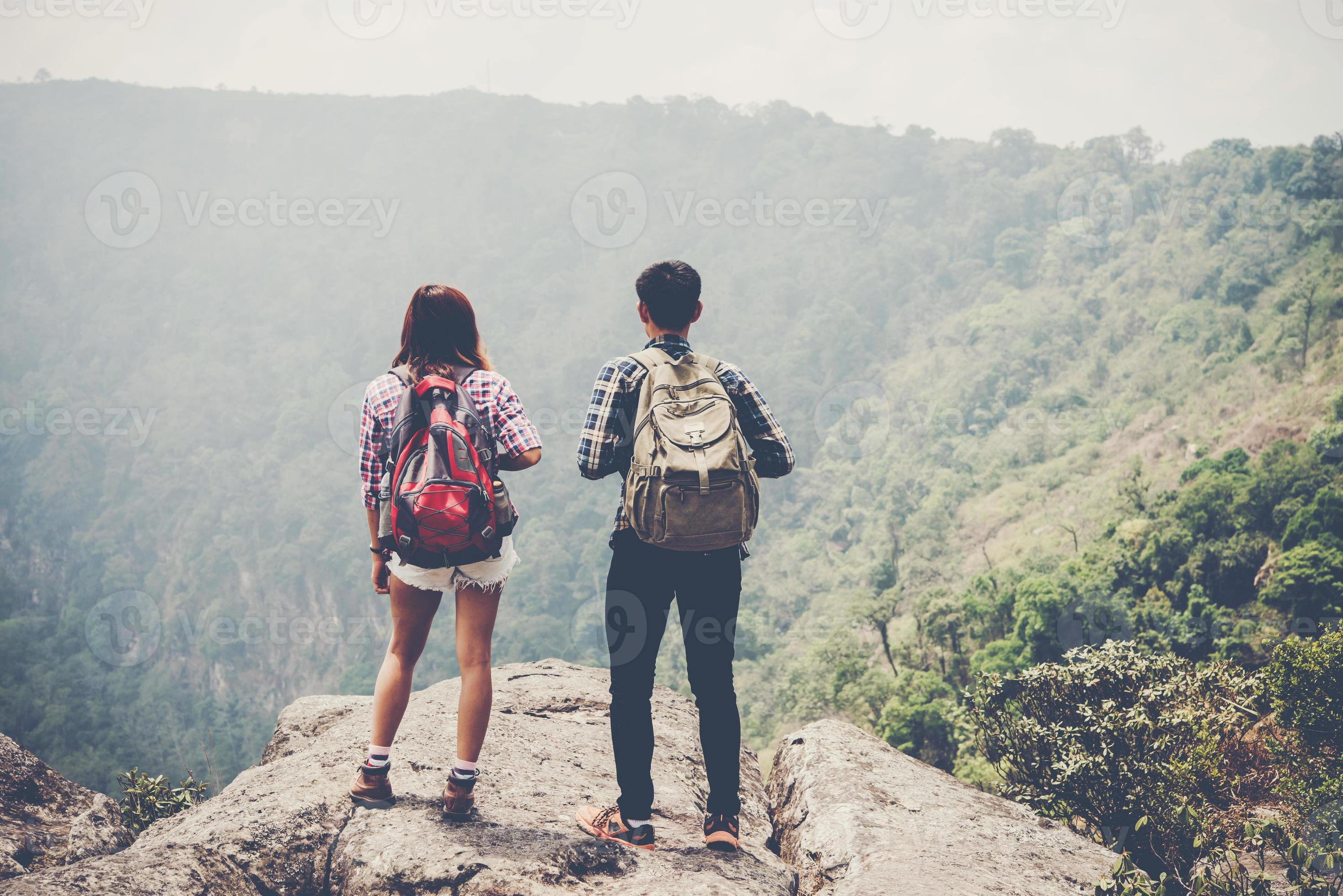 Hiker couple with backpacks standing on top of a mountain and enjoying nature view photo