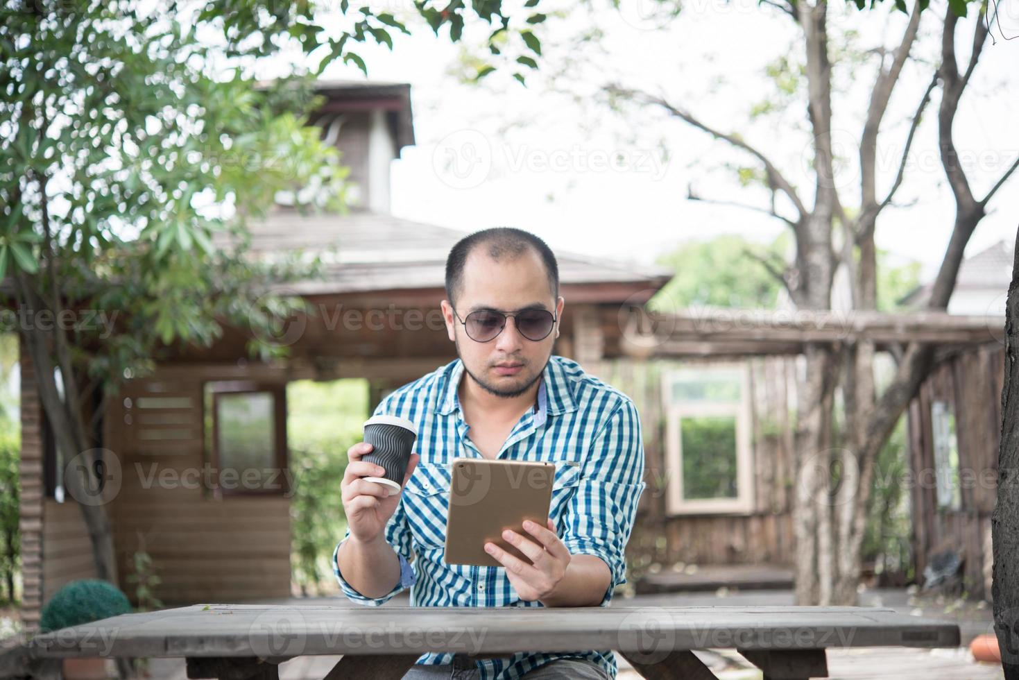 Young man sits outdoors at a wooden table and relaxing with tablet photo