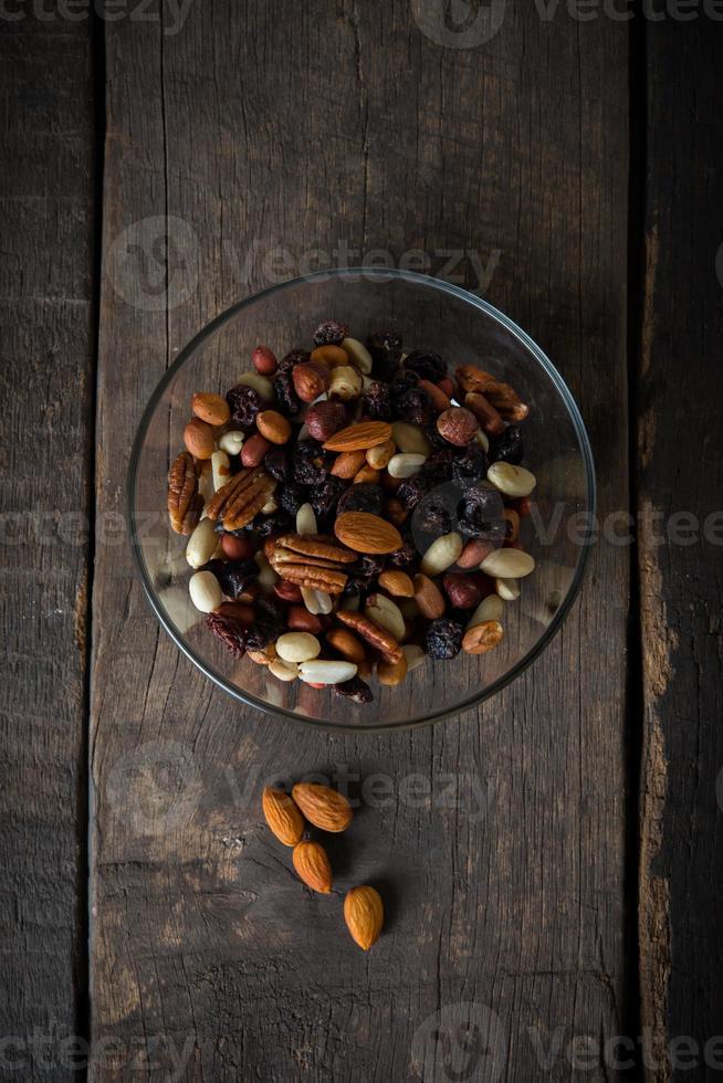 Nueces mixtas vertiendo de un recipiente sobre fondo de madera foto