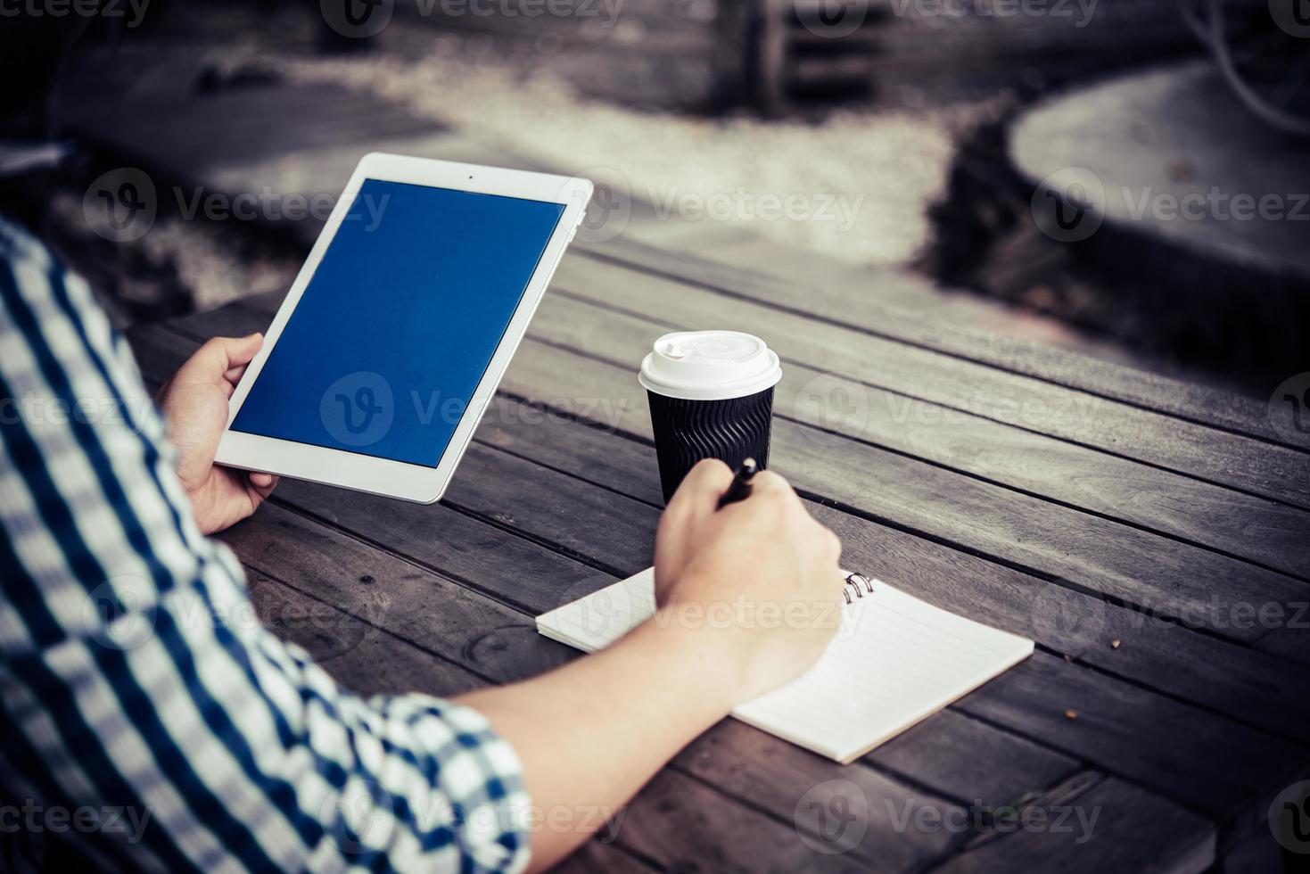 Joven con tableta digital mientras bebe café sentado en el jardín de su casa foto