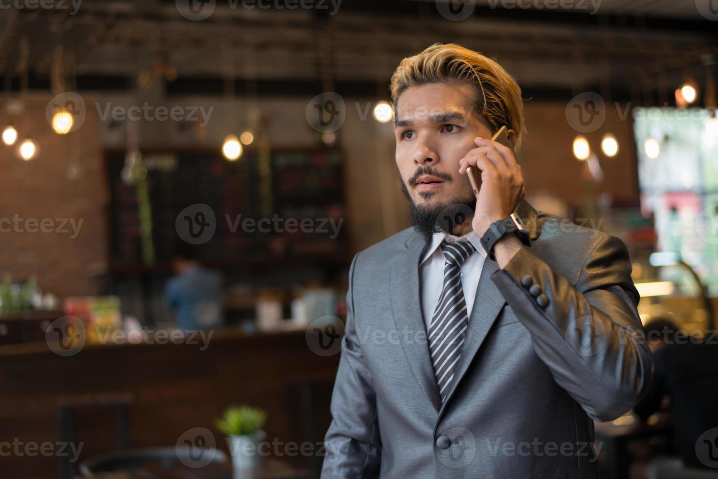 Apuesto hombre de negocios hablando por teléfono mientras se toma un descanso en el café foto