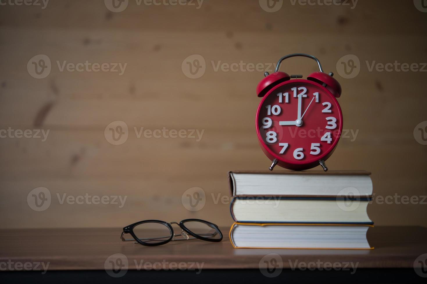 Despertador a las 9 de la mañana en la pila de libros con gafas en la mesa de madera foto