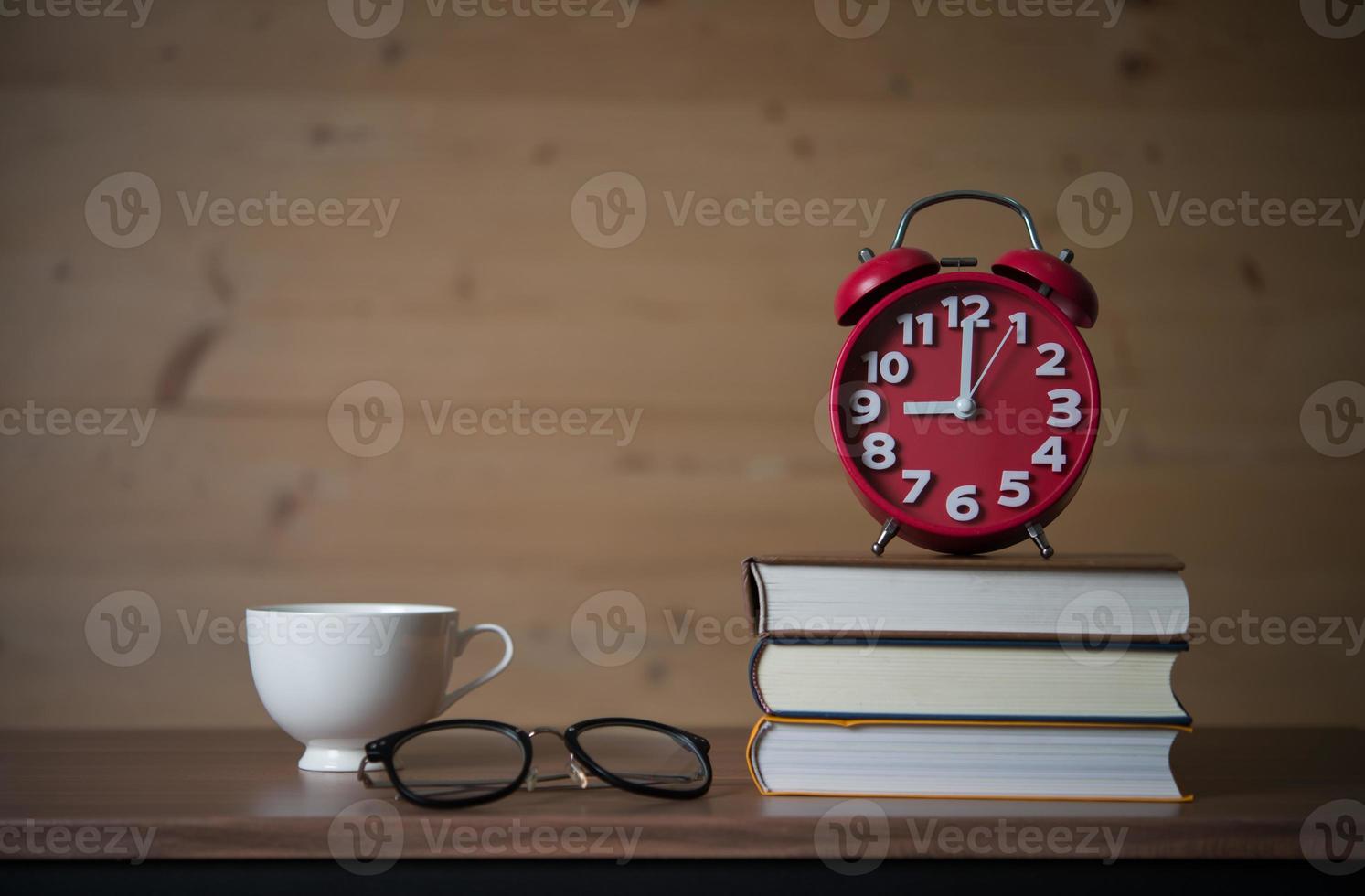 Despertador a las 9 de la mañana en una pila de libros con vasos y una taza de café en la mesa de madera foto