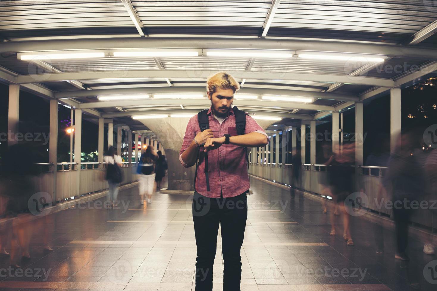 Handsome bearded man standing on the street while looking at smartwatch traveling at night photo