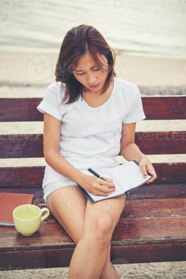 Hermosa joven escribiendo en el bloc de notas mientras está sentado en un banco foto